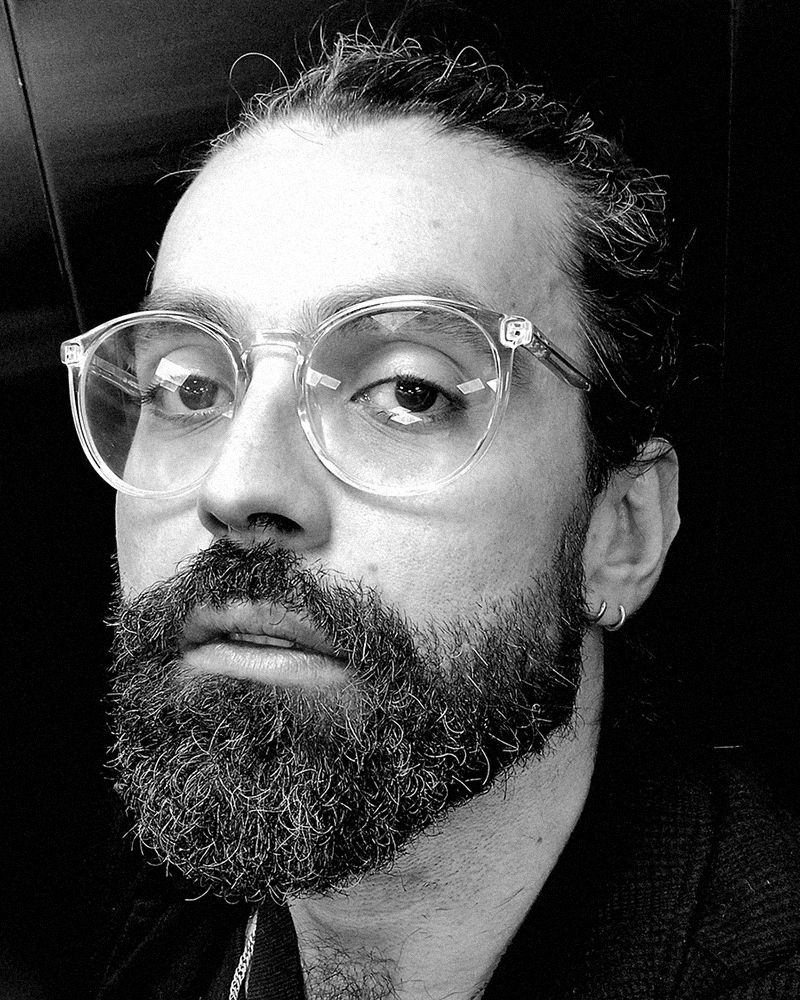 Retrato de Luca(s) Brandão em preto e branco, de óculos e barba cheia